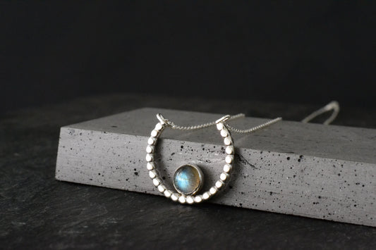 crescent moon Necklace with a central labradorite gemstone pendant on a dark surface